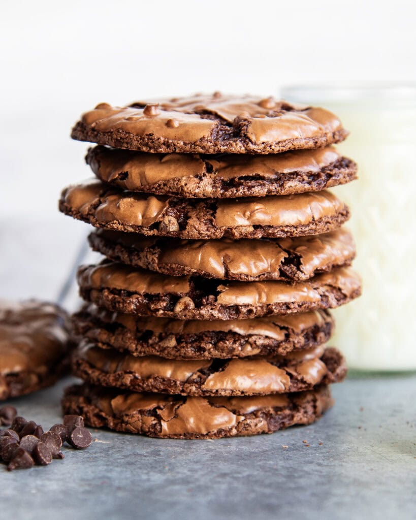 A stack of thin and chewy flourless chocolate cookies next to a cup of milk.