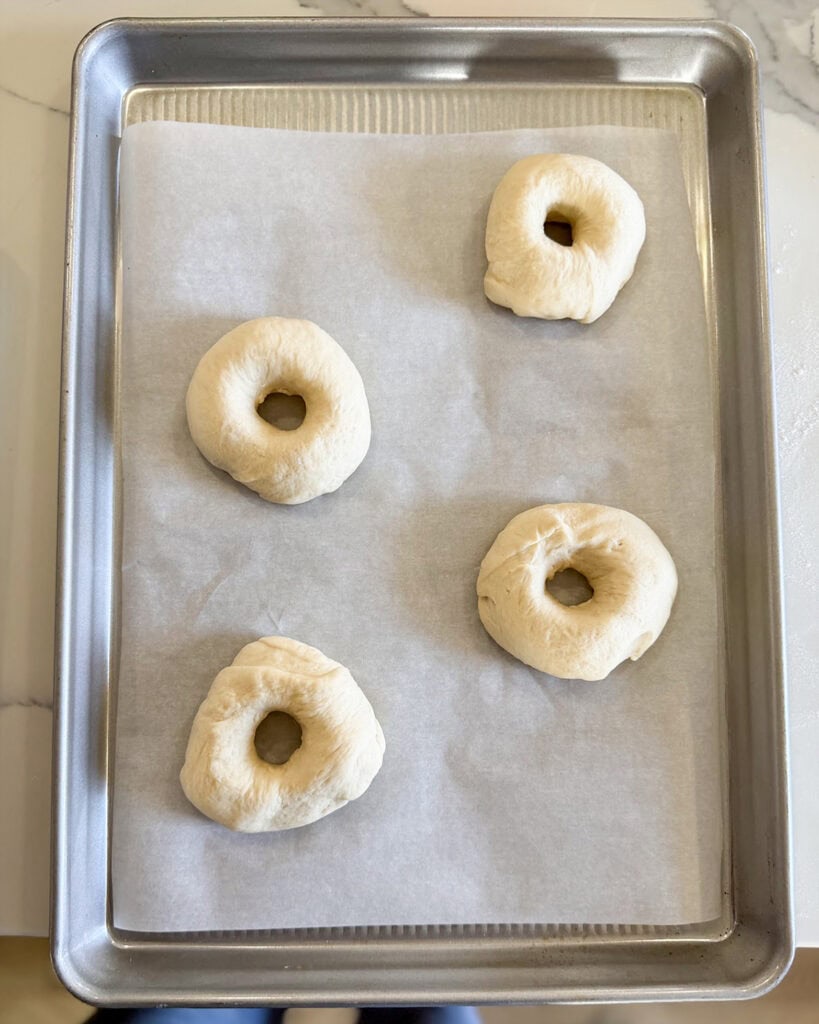 Four shaped bagels on a cookie sheet.