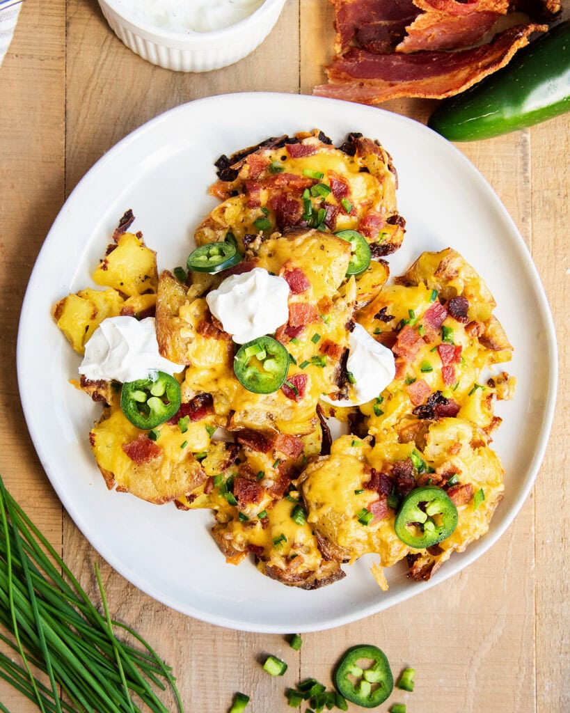 A plate of jalapeno popper smashed potatoes, and some are topped with sour cream.