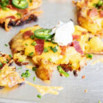 A close up of a crispy smashed potato topped with cheese, bacon, jalapenos, chives, and sour cream.