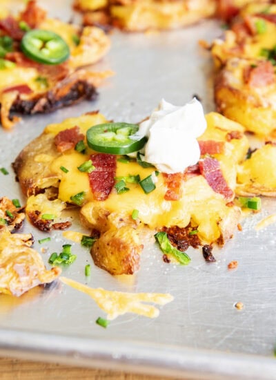 A close up of a crispy smashed potato topped with cheese, bacon, jalapenos, chives, and sour cream.