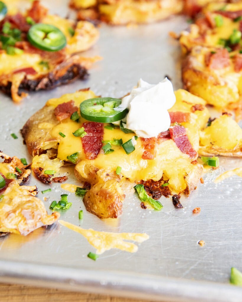 A close up of a crispy smashed potato topped with cheese, bacon, jalapenos, chives, and sour cream. 