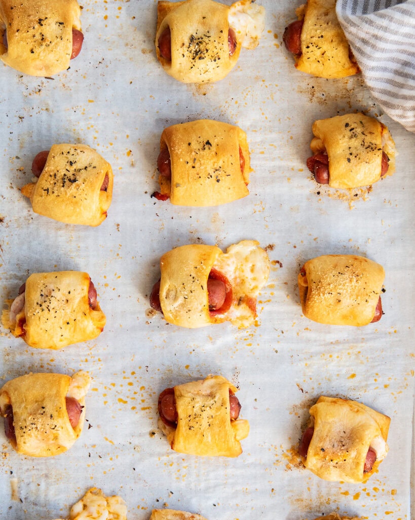 Rows of pizza pigs in a blanket on a cookie sheet.