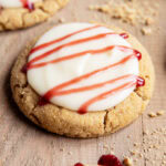 A Raspberry cheesecake cookie with cream cheese frosting, and a drizzle of raspberry sauce on top.