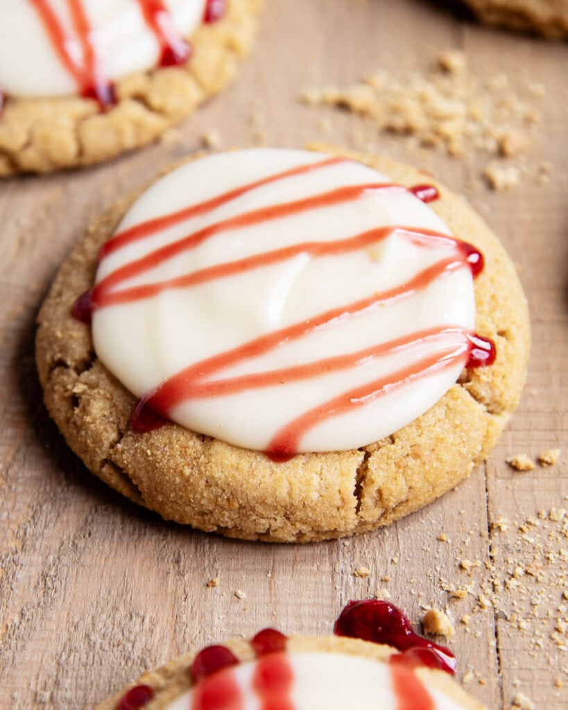 A Raspberry cheesecake cookie with cream cheese frosting, and a drizzle of raspberry sauce on top.