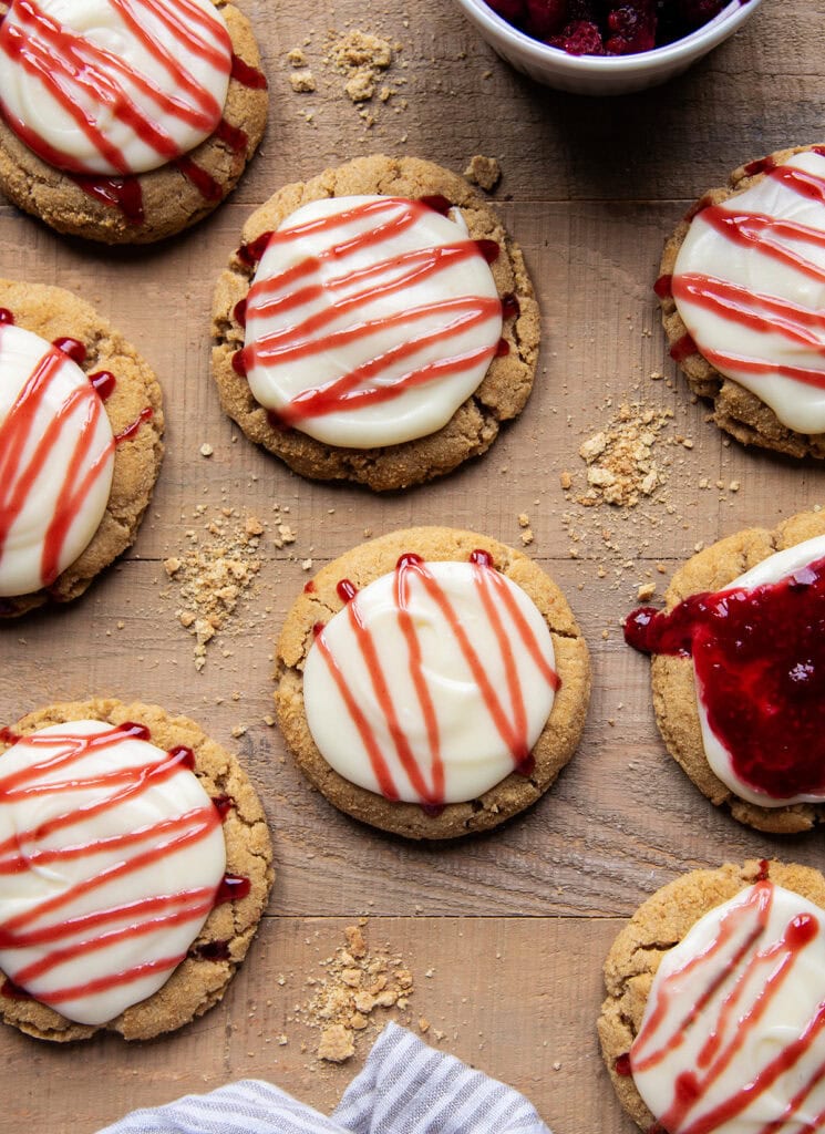 A baking tray of A Raspberry cheesecake cookies with cream cheese frosting, and a drizzle of raspberry sauce on top.