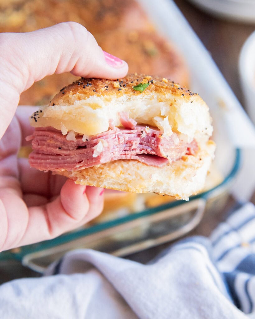 A hand holding a slider sandwich full of corned beef and sauerkraut, with a bite out of the front of it.