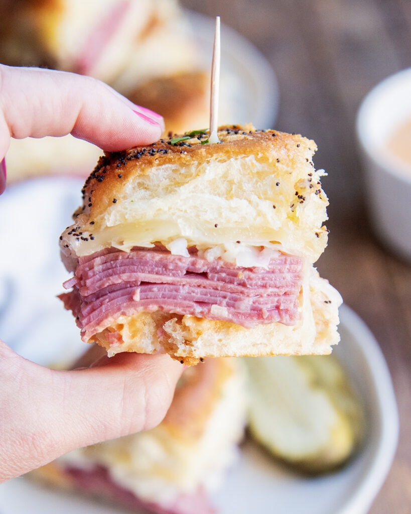 A hand holding a slider sandwich full of corned beef and sauerkraut. 