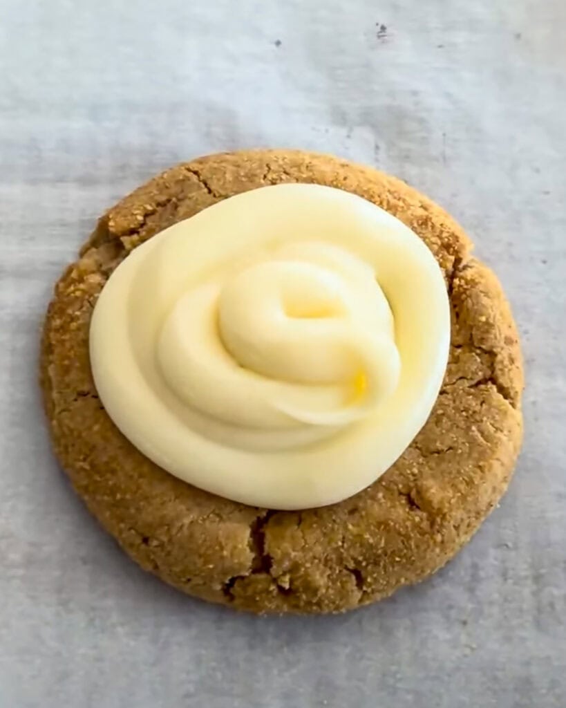 A cream cheese frosted graham cracker cookie on a piece of parchment paper.