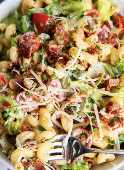 A close up of a bowl of BLT pasta salad with bacon, lettuce, tomatoes, and parmesan cheese.