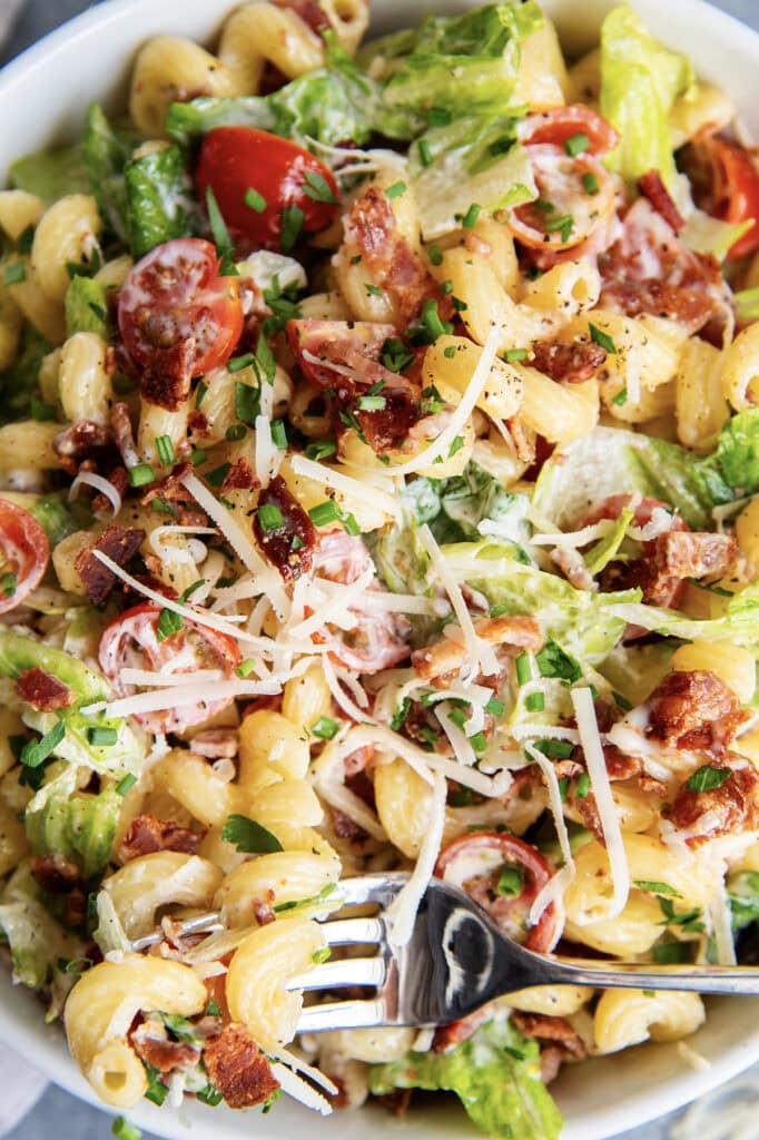 A close up of a bowl of BLT pasta salad with bacon, lettuce, tomatoes, and parmesan cheese. 