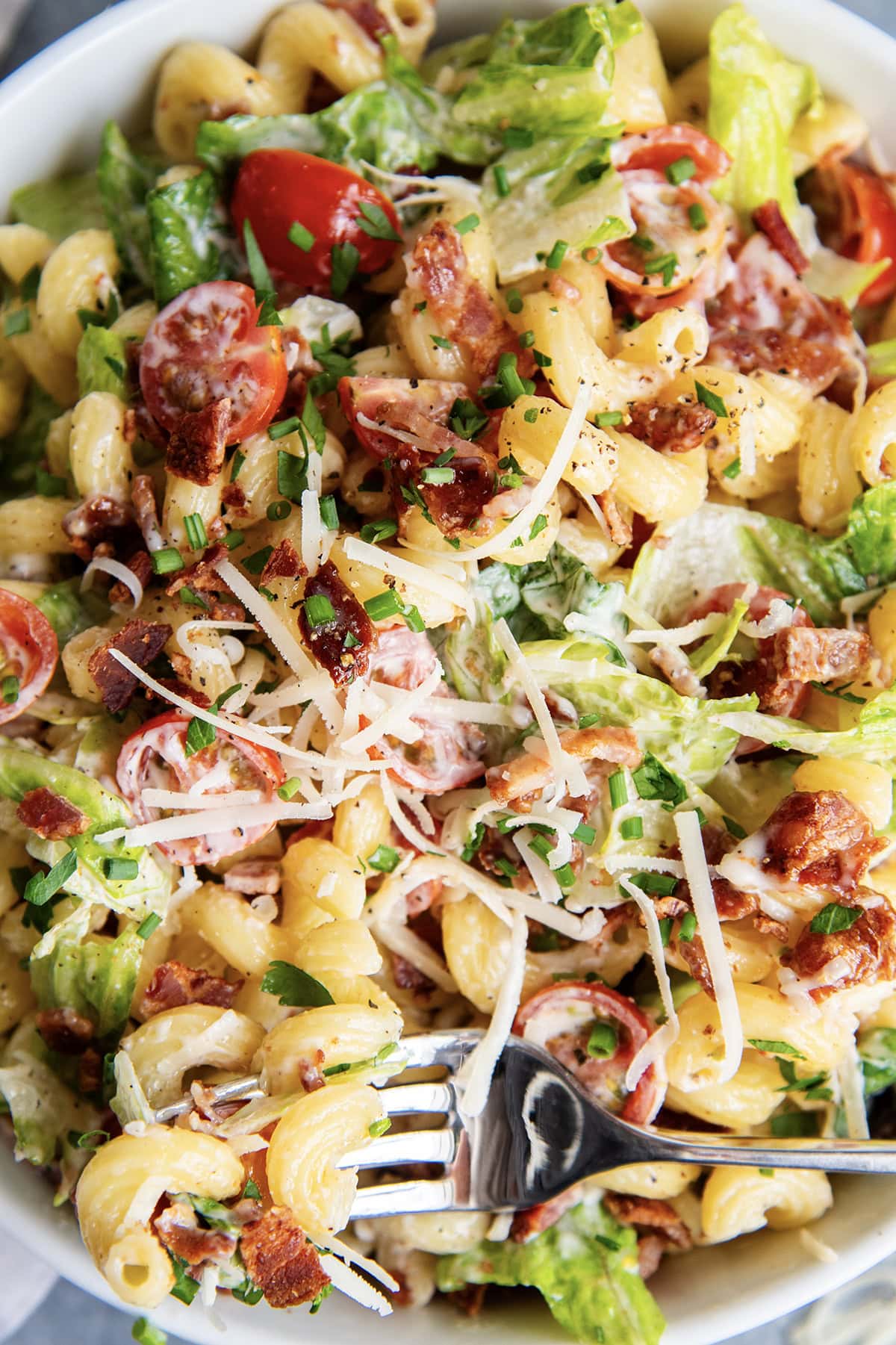 A close up of a bowl of BLT pasta salad with bacon, lettuce, tomatoes, and parmesan cheese.