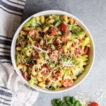 An above view of a bowl of BLT pasta salad with lettuce, tomatoes, cavatappi pasta, and parmesan cheese.