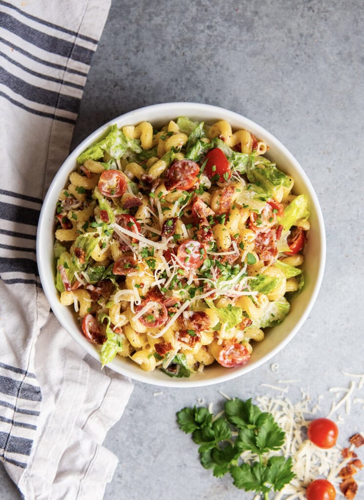 An above view of a bowl of BLT pasta salad with lettuce, tomatoes, cavatappi pasta, and parmesan cheese.