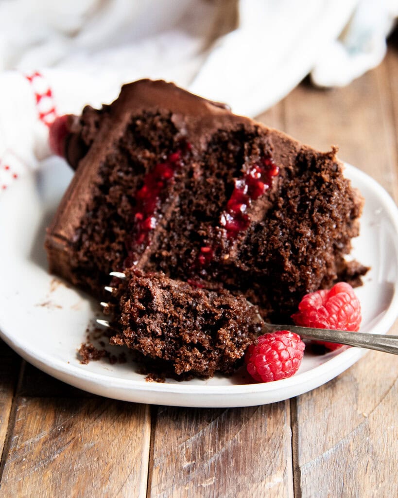 A slice of chocolate raspberry cake on a plate with a forkful cut out.
