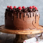 A three layer chocolate raspberry cake on a wooden cake stand.
