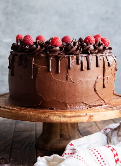 A three layer chocolate raspberry cake on a wooden cake stand.