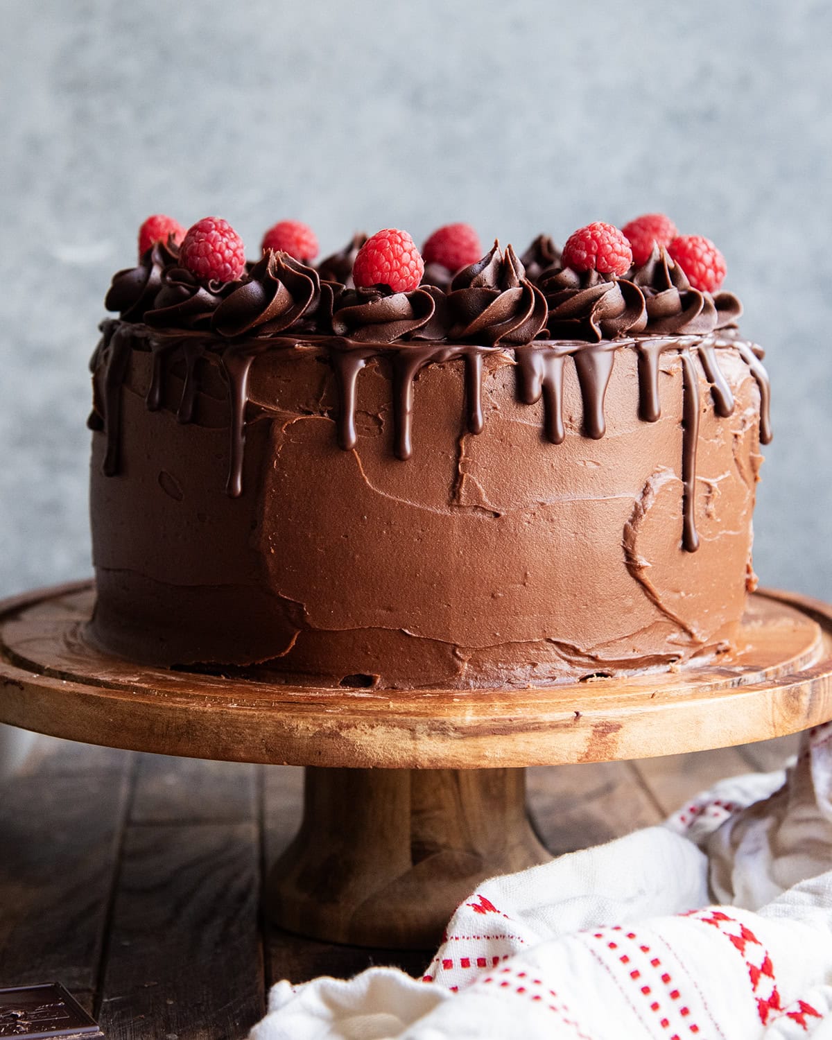 A three layer chocolate raspberry cake on a wooden cake stand.