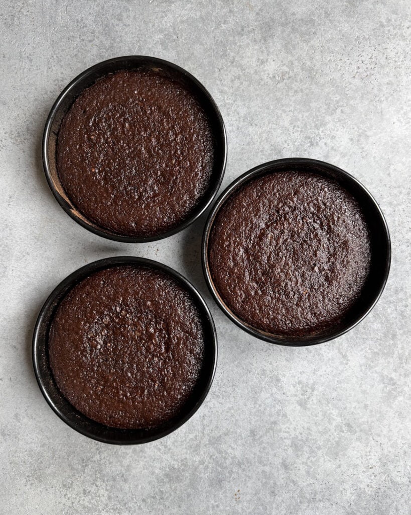 Three layers of chocolate cake in cake pans.
