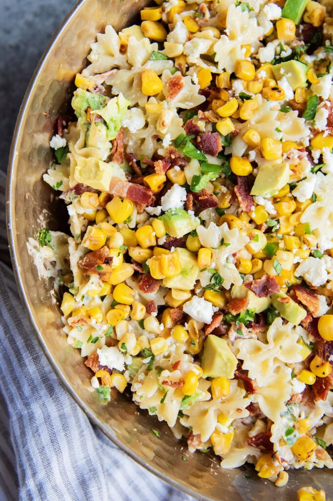 A close up of a bowl of Mexican street corn pasta salad loaded with corn, bacon, cotija, and avocado.