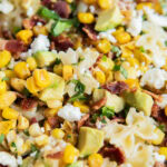 A close up of a bowl of Mexican street corn pasta salad loaded with corn, bacon, cotija, and avocado.
