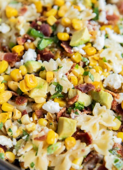 A close up of a bowl of Mexican street corn pasta salad loaded with corn, bacon, cotija, and avocado.