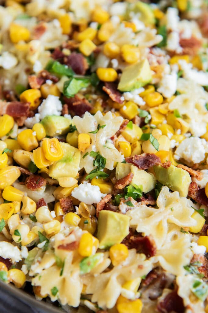 A close up of a bowl of Mexican street corn pasta salad loaded with corn, bacon, cotija, and avocado.