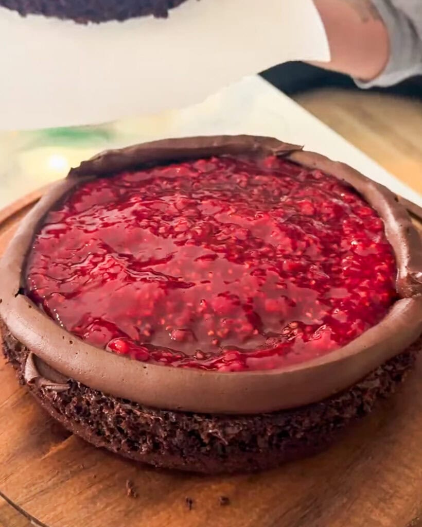 A layer of chocolate cake topped with a border of chocolate buttercream frosting, and raspberry filling.