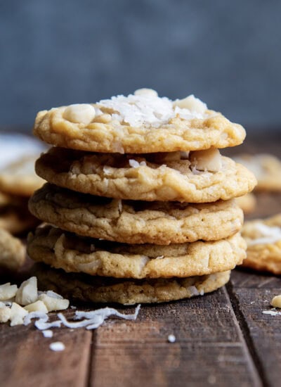 A stack of five coconut macadamia nut cookies, the top cookie has shredded coconut on top.