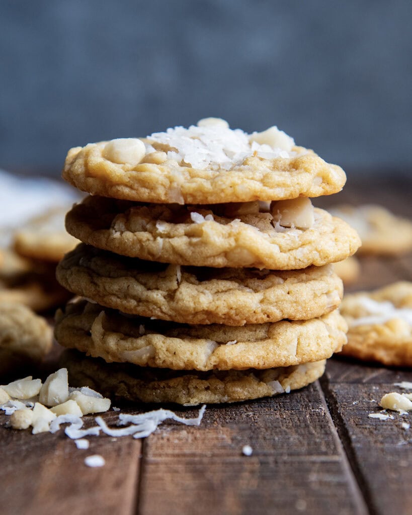 A stack of five coconut macadamia nut cookies, the top cookie has shredded coconut on top.