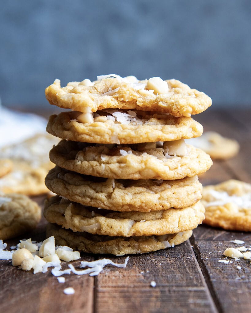 A stack of six coconut macadamia nut cookies, the top cookie has a bite out of it.