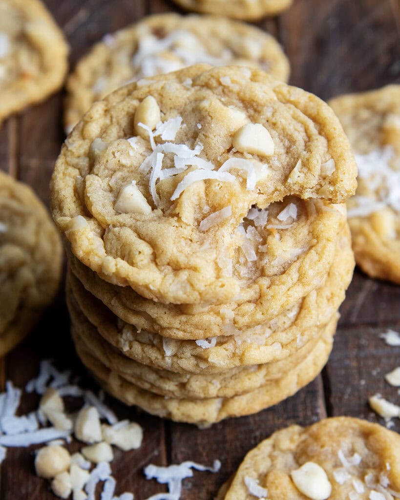 A stack of six coconut macadamia nut cookies, the top cookie has a bite out of it.