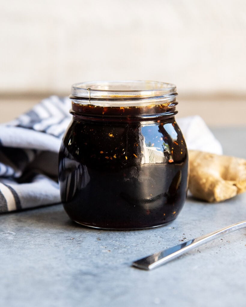 A jar of homemade teriyaki sauce with pieces of garlic and ginger in it.