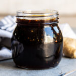 A jar of homemade teriyaki sauce with pieces of garlic and ginger in it.