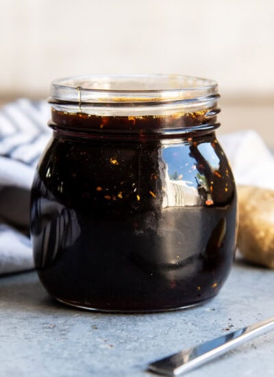 A jar of homemade teriyaki sauce with pieces of garlic and ginger in it.