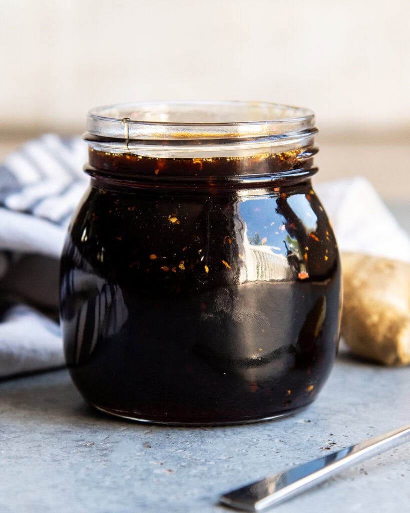 A jar of homemade teriyaki sauce with pieces of garlic and ginger in it.
