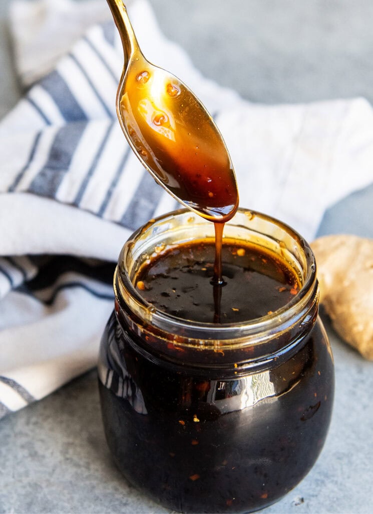 A spoon drizzling teriyaki sauce into a jar of it.