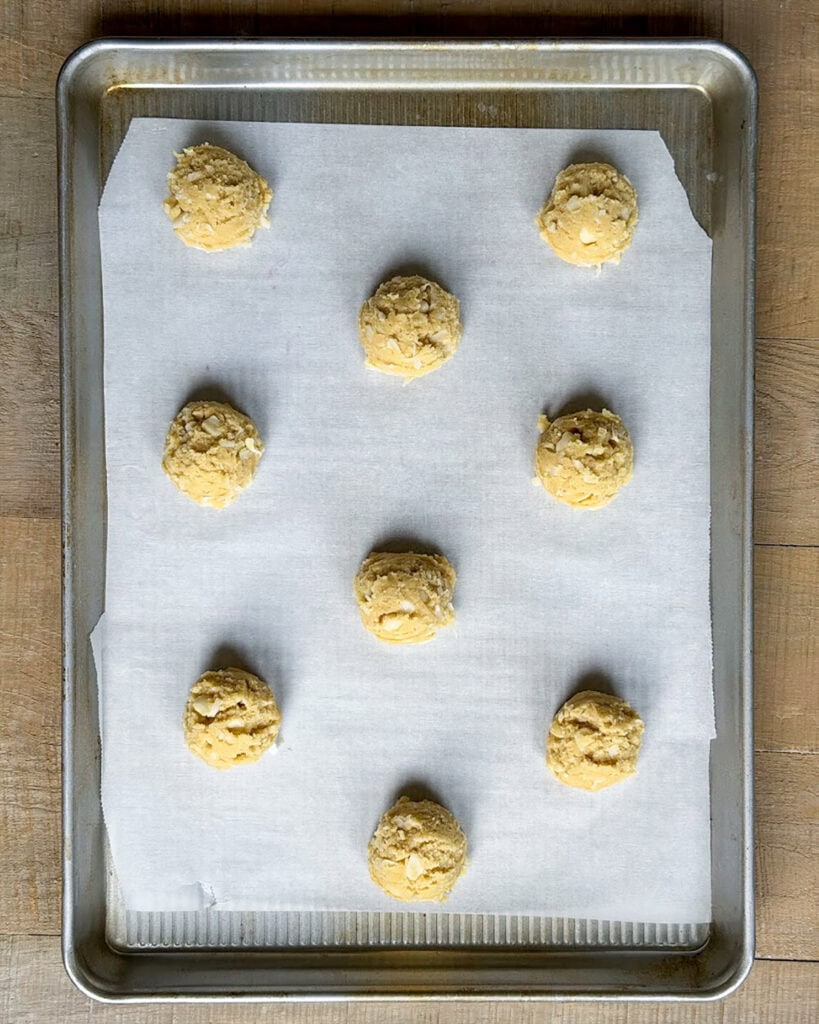 Coconut macadamia nut cookie dough balls on a cookie sheet.