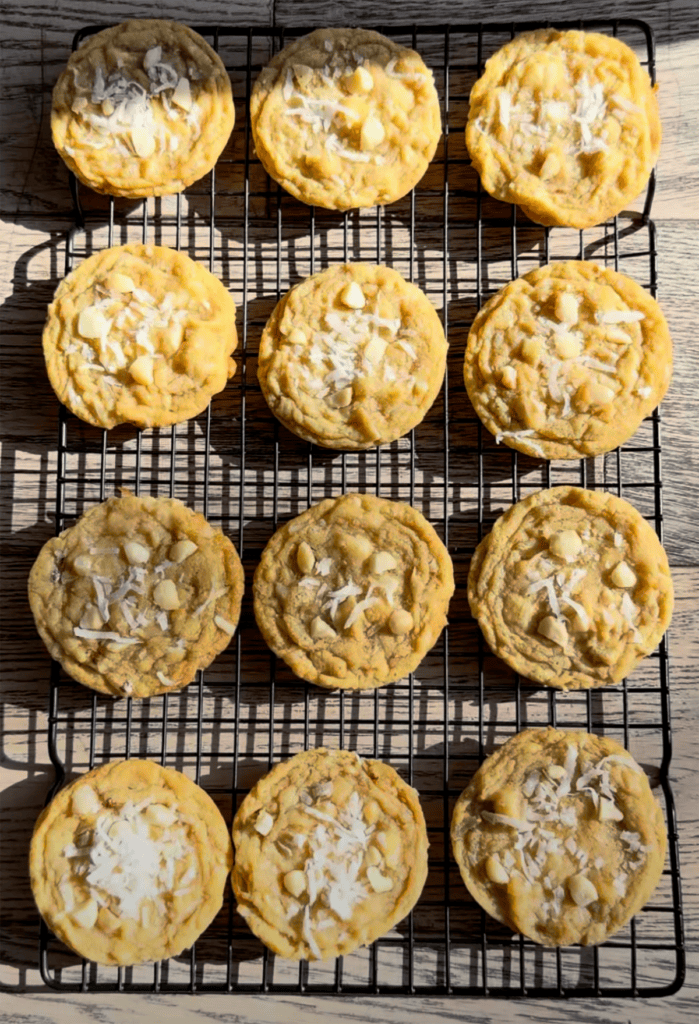An above view of coconut macadamia nut cookies with shredded coconut on top on a wire rack.