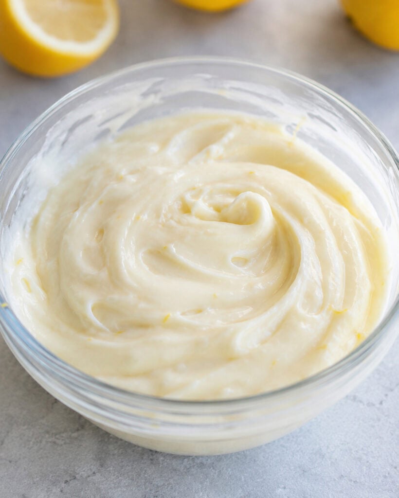 A glass bowl of lemon cream pie filling, its a white creamy mixture with lemon zest bits in it.