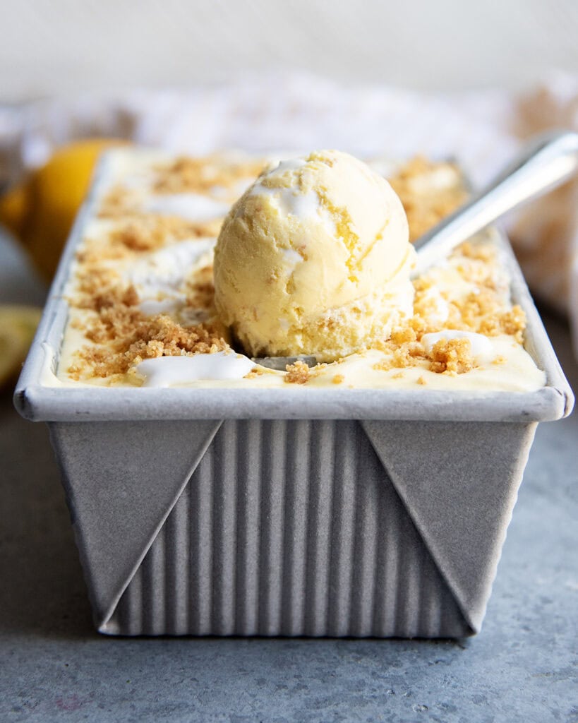 A scoop of lemon ice cream in a bread pan container of lemon ice cream.