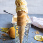 Two scoops of lemon cream pie ice cream on an ice cream cone, set in a glass jar.