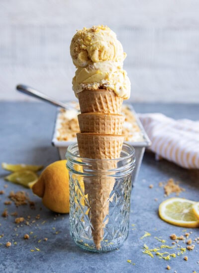 Two scoops of lemon cream pie ice cream on an ice cream cone, set in a glass jar.