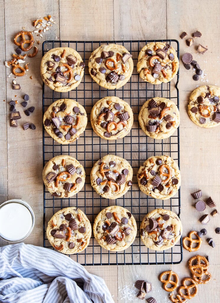 An above view of a cookie sheet lined with peanut butter pretzel cookies topped with chocolate chips and peanut butter cups.