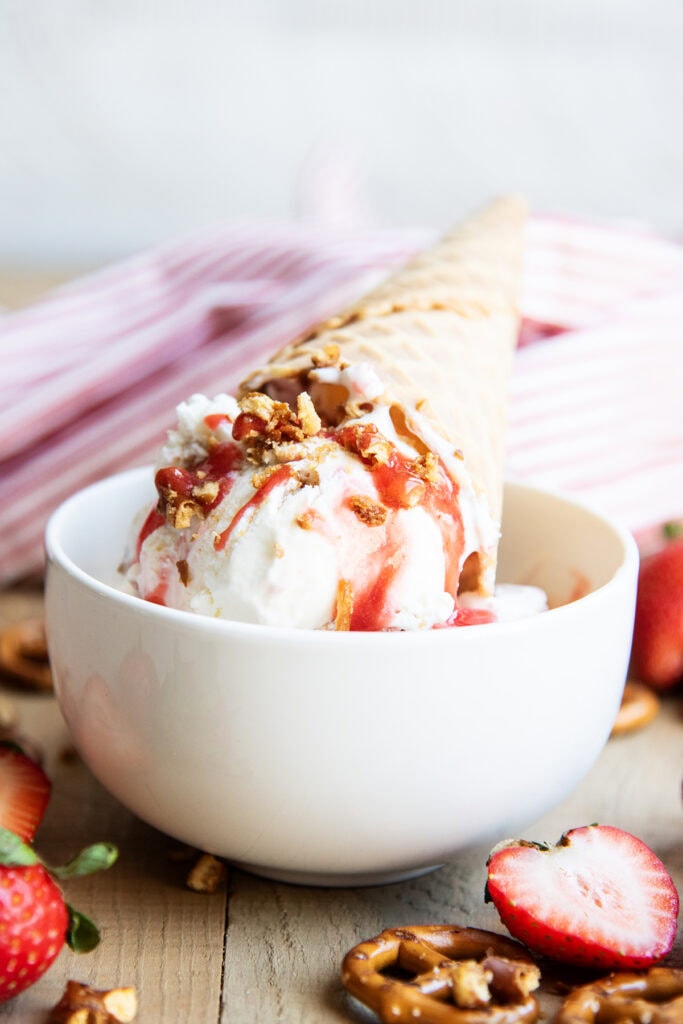 A bowl of strawberry pretzel salad ice cream with a cone on top.
