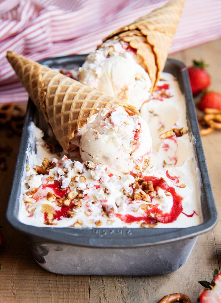 Two cheesecake ice cream cones on a pan of the ice cream, with strawberry swirls in the ice cream.