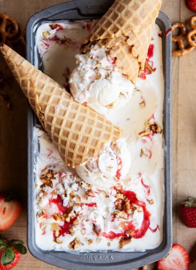 Two cheesecake ice cream cones on a pan of the ice cream, with strawberry swirls in the ice cream.