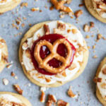 An above view of a cookie topped with cream cheese frosting, strawberry sauce and a mini pretzel.
