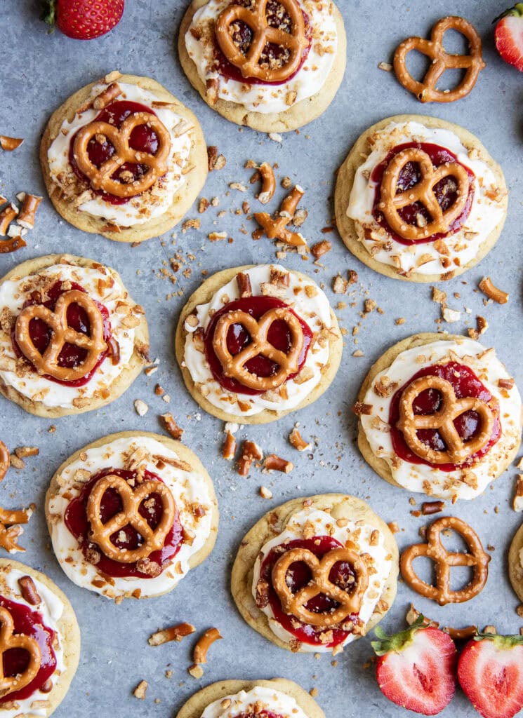An above view of a bunch of strawberry pretzel salad cookies, they are An above view of a cookies topped with cream cheese frosting, strawberry sauce and a mini pretzel.