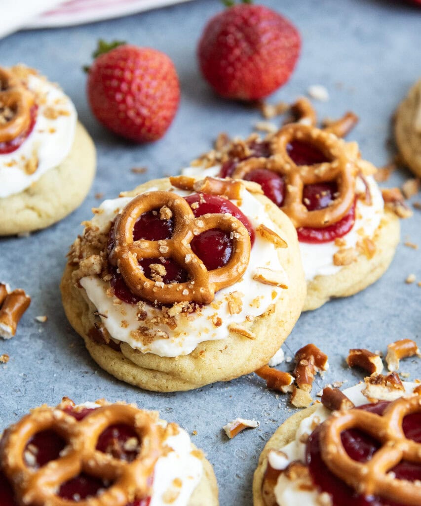 An above view of a bunch of strawberry pretzel salad cookies, they are An above view of a cookies topped with cream cheese frosting, strawberry sauce and a mini pretzel.